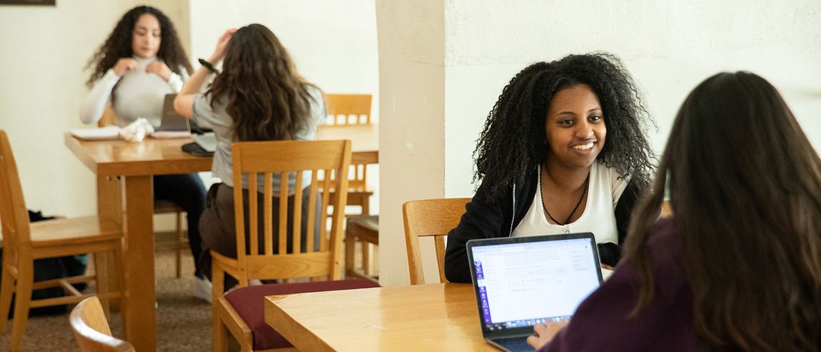 four students sitting at tables talking and studying