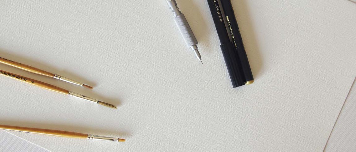 Paintbrushes and pens on top of a canvas
