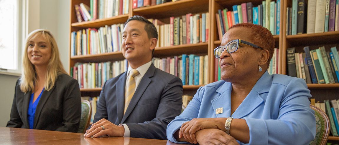 three people sitting at a desk in a library