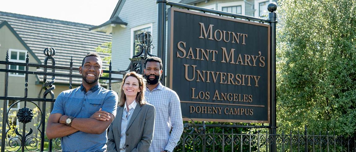 three graduate students smiling in front of campus sign