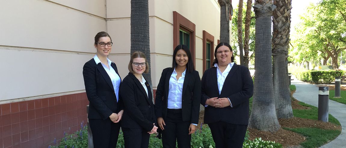 group of four students in professional attire smiling on campus