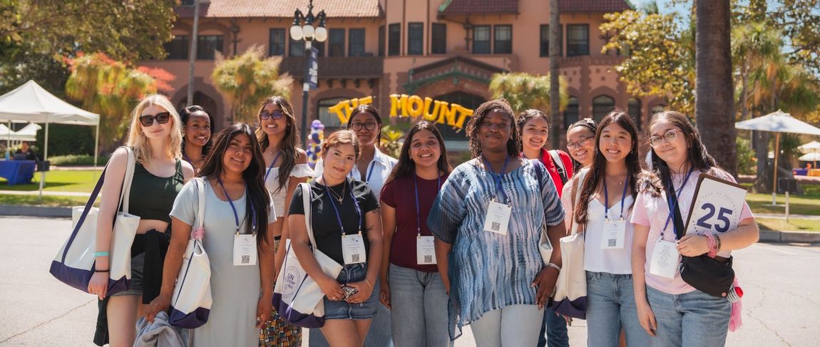 group of female students with lanyards at a campus event smiling in front of the doheny mansion