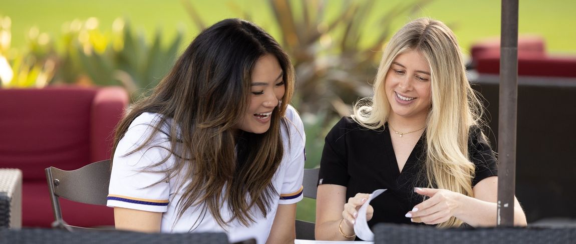 two female nursing students sitting outside working together looking at a notebook