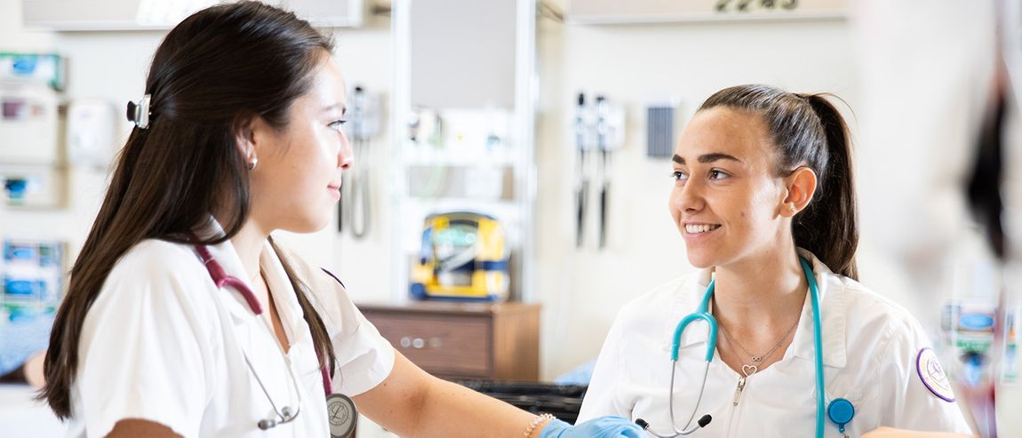 two students in white coats working in a lab smiling at each other