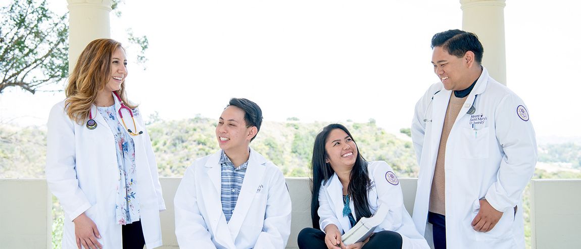 group of four students sitting in an outside corridor at chalon campus in white coats smiling