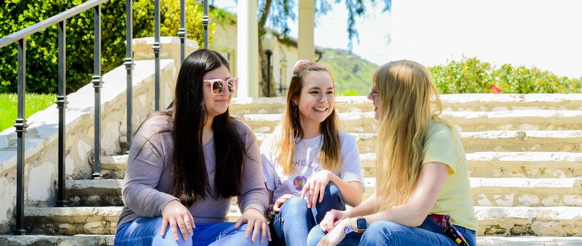 three female students sitting on campus steps talking in jeans and msmu shirts