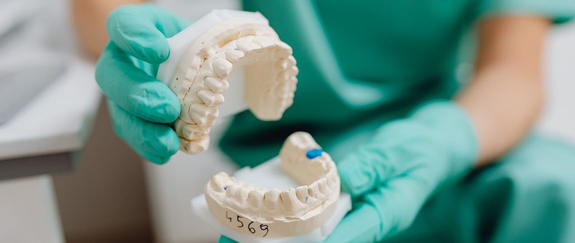 fake teeth being held up by a worker in teal green scrubs and gloves