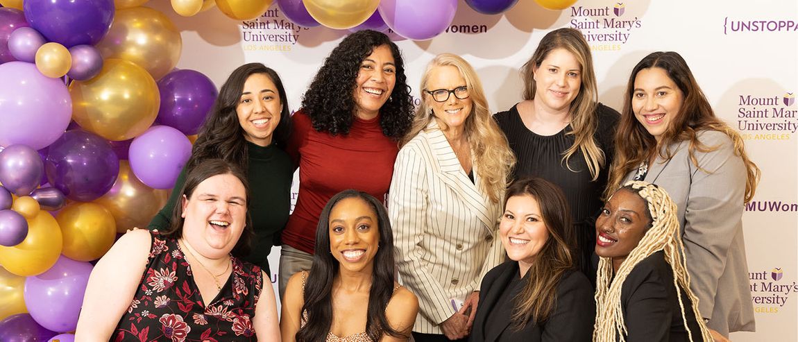 Group of alums smiling in group photo in front of balloon arch and 91ɬ�� backdrop