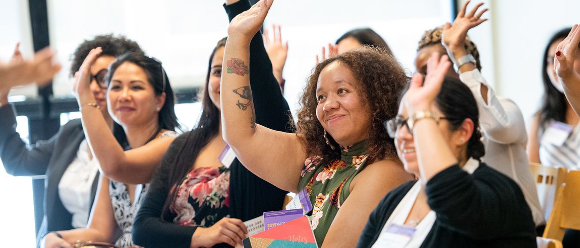 women listening to a presentation raising their hands