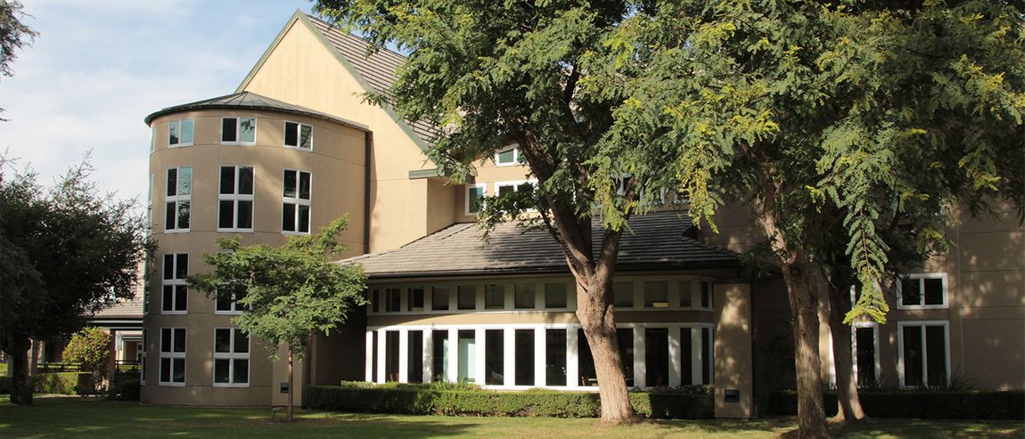 A rounded building with large windows seen through tall trees.