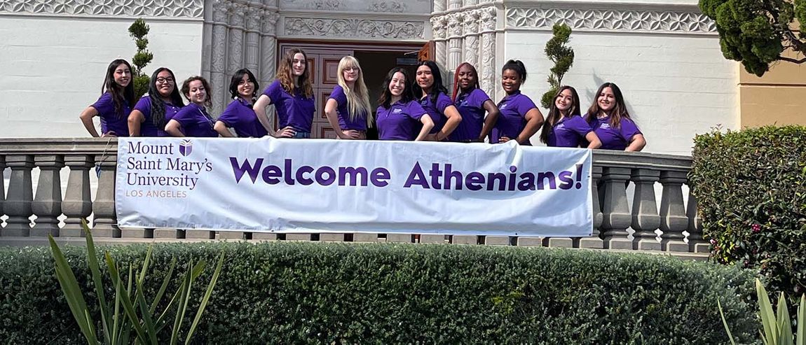 91ɬ�� students standing in front of Mary Chapel smiling with a Welcome Athenians sign