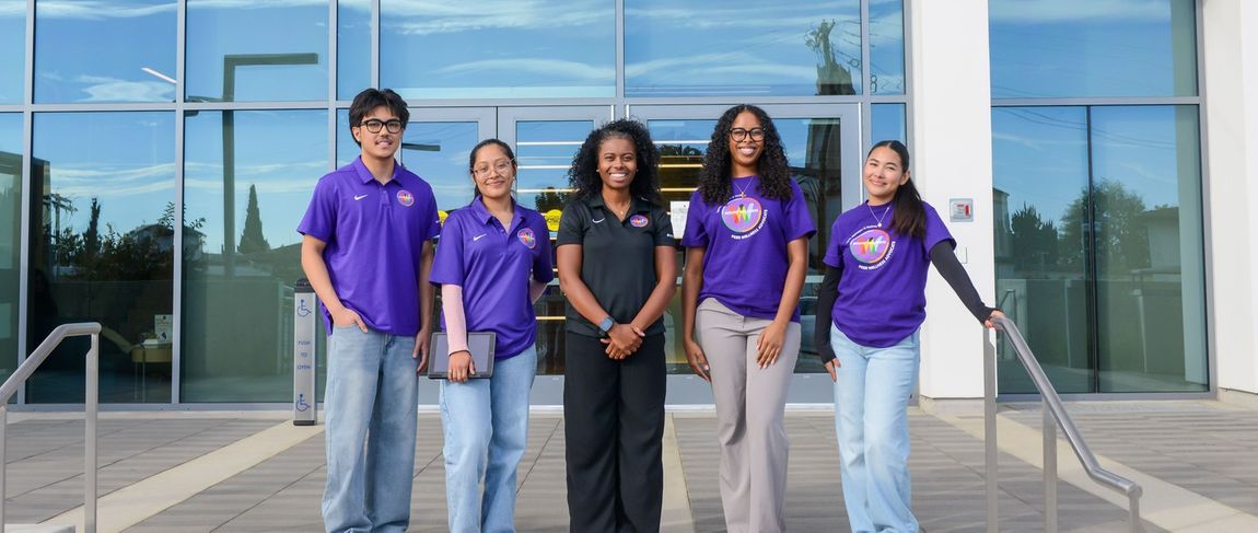 group of wellness students in purple polos standing in front of the entrance to the wellness pavilion