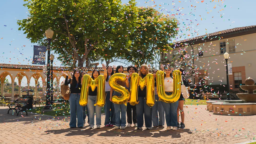 Students holding balloons spelling out ������ý with confetti raining down on them