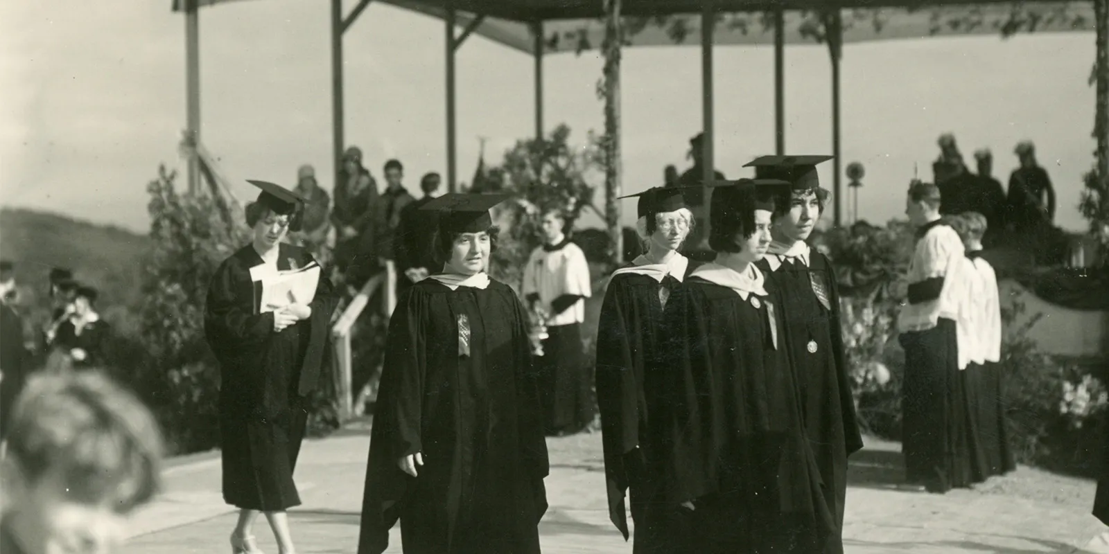 Black and white photo of students from 1929 in graduation regalia standing outside in a group