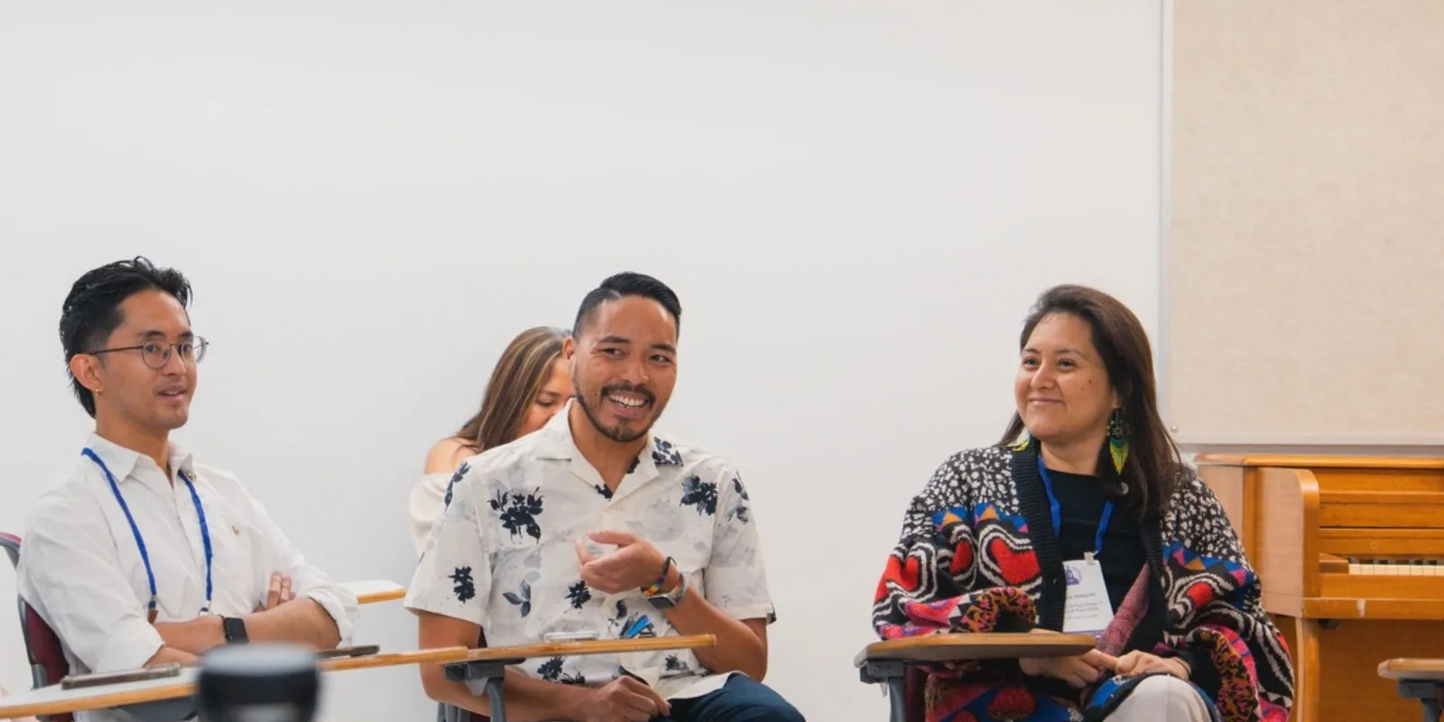 graduate students sitting at desks smiling and talking with a white background