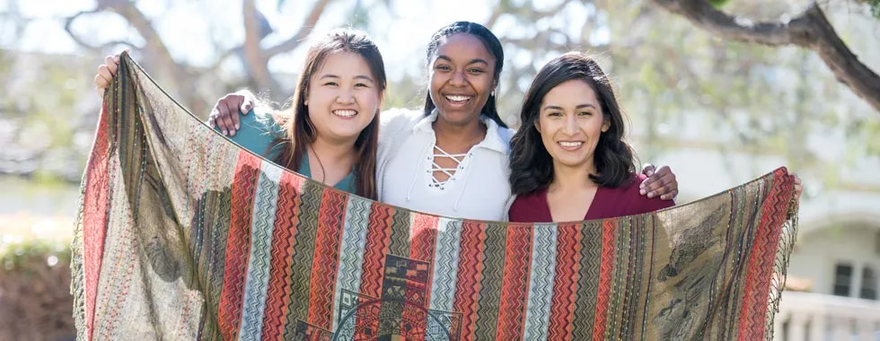 Pauline Cheng ’19, Janae Jones ’19 and Erica Cisneros ’18 hold up a woven blanket made in Peru.