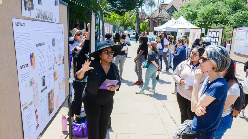 Student researcher Brooke Johnson presents her poster at Rose Hills Plaza during Mount Saint Mary’s University’s 2025 Academic Symposium, engaging attendees in a discussion about her findings.