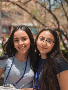 two female students, one in grey and one in black, smiling together on campus