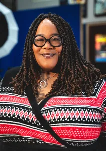 womain in red, white, and black blouse smiling, wearing glasses