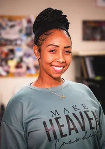 Woman in teal shirt that says make heaven crowded smiling at the camera