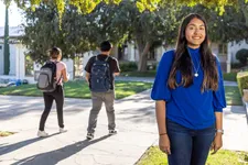 female student in cobalt blue shirt and long brown hair smiling, with two students with backpacks walking away in the background