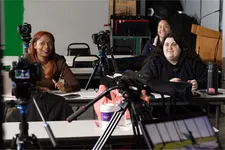 three students sitting in class listening with film equipment