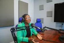 female student in green jacket and black shirt, talking into microphone seated a table
