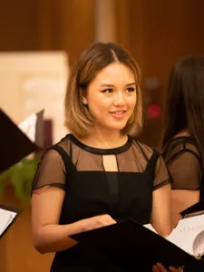 female student smiling in black dress holding a black music sheet binder