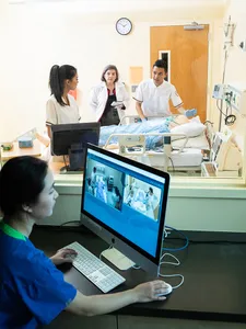 students working in lab with dummy patient while someone monitors from computer