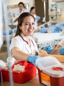 female student in nursing lab smiling as they work on practicing iv insertions