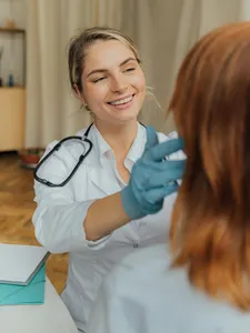 female doctor or nurse smiling as they touch a patient's head with blue gloves on for evaluation