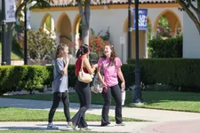 three students laughing as they walk on a campus path outdoors