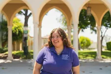 student in purple ÿ�մ������ shirt smiling in front of an outside arched corridor