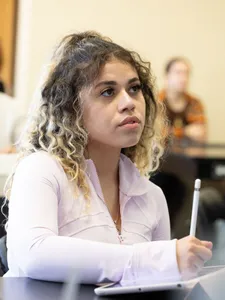 female student in light pink long sleeve listening in class taking notes