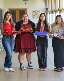 four female students smiling in outside corridor holding mass elements