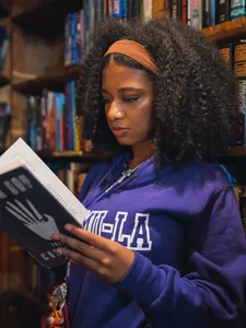female student in purple ÿ�մ������ hoodie and orange hairband standing in bookstore reading a book