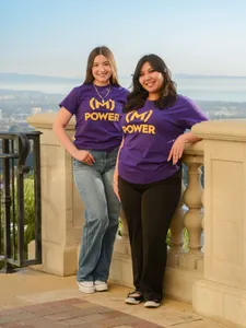 two female students smiling standing outdoors back to pack in purple m-power shirts