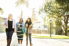 three female students walking and smiling on campus