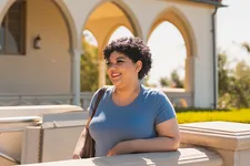 A student leaning against a wall on Chalon Campus with arches in the background.