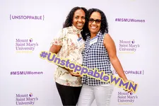 two women smiling in front of backdrop with a Unstoppable women hashtag sign