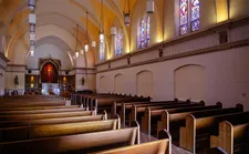 The inside of a long, narrow chapel with the dais in at the end, seen over rows of pews.