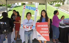 Two students holding up signs related to voting at an event booth.