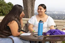 Two students sitting around table outside and laughing.