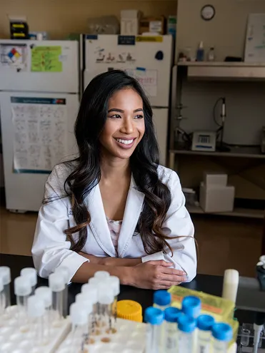 female lab student smiling working in lab sitting at desk with equipment