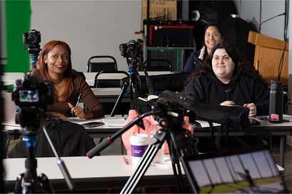 three students sitting in class listening with film equipment