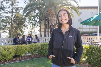 student in black jacket smiling outdoors with students walking behind them