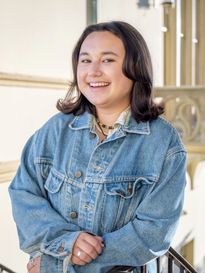 student smiling with brown shoulder-length hair and wearing a jean jacket