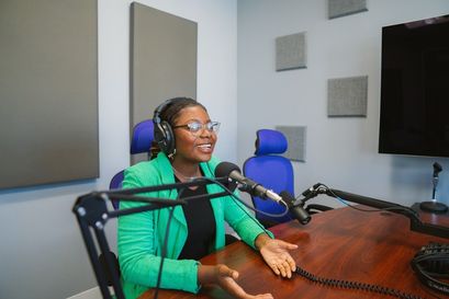 female student in green jacket and black shirt, talking into microphone seated a table