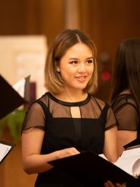 female student smiling in black dress holding a black music sheet binder