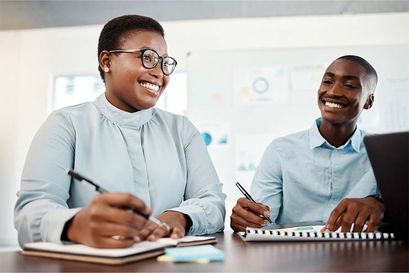 two people smiling working together at a table with notepads